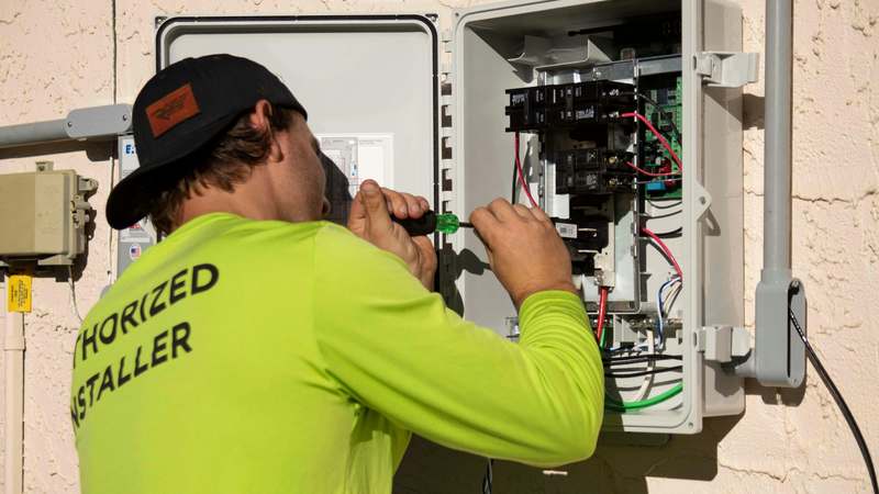 Close-up of a technician inspecting a cracked solar panel on a residential rooftop, wearing gloves and safety glasses, with tools visible in background